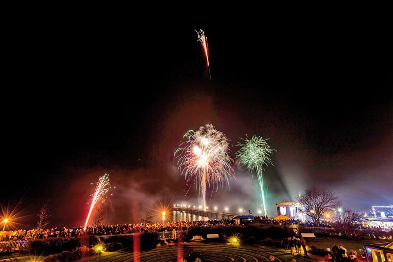 Nachtaufnahme eines Feuerwerks über einer Menschenmenge an einer beleuchteten Brücke.