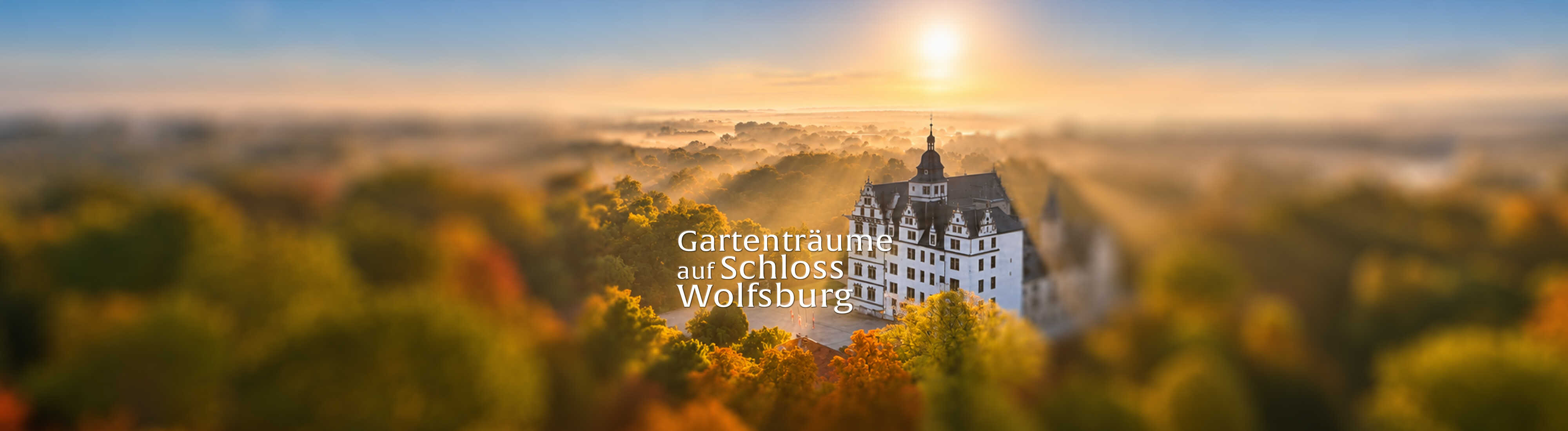 Das Bild zeigt Schloss Wolfsburg inmitten herbstlich gefärbter Natur bei warmem Morgenlicht mit der Aufschrift „Gartenträume auf Schloss Wolfsburg“.