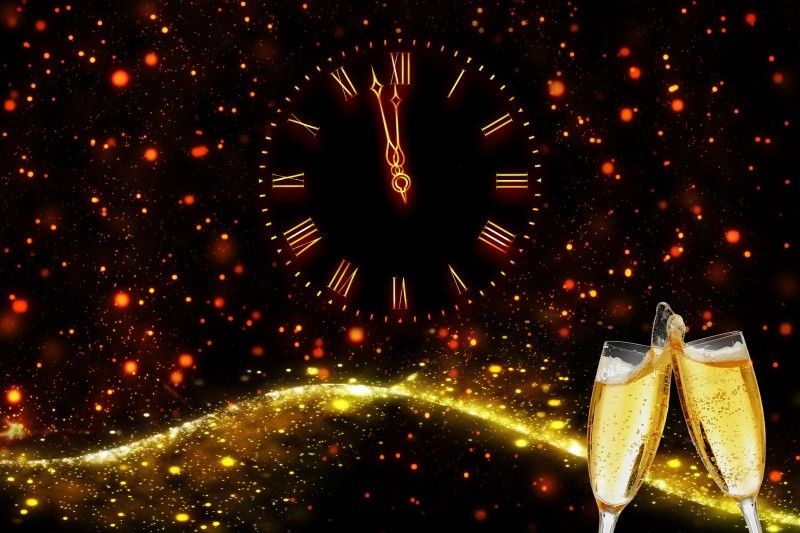 Eine Uhr zeigt Mitternacht in festlicher Atmosphäre mit funkelnden Lichtern und zwei anstoßenden Champagnergläsern.