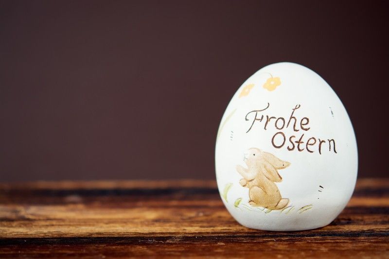 Dekoratives Osterei mit der Aufschrift 'Frohe Ostern' und einem Hasenmotiv auf einem Holztisch.