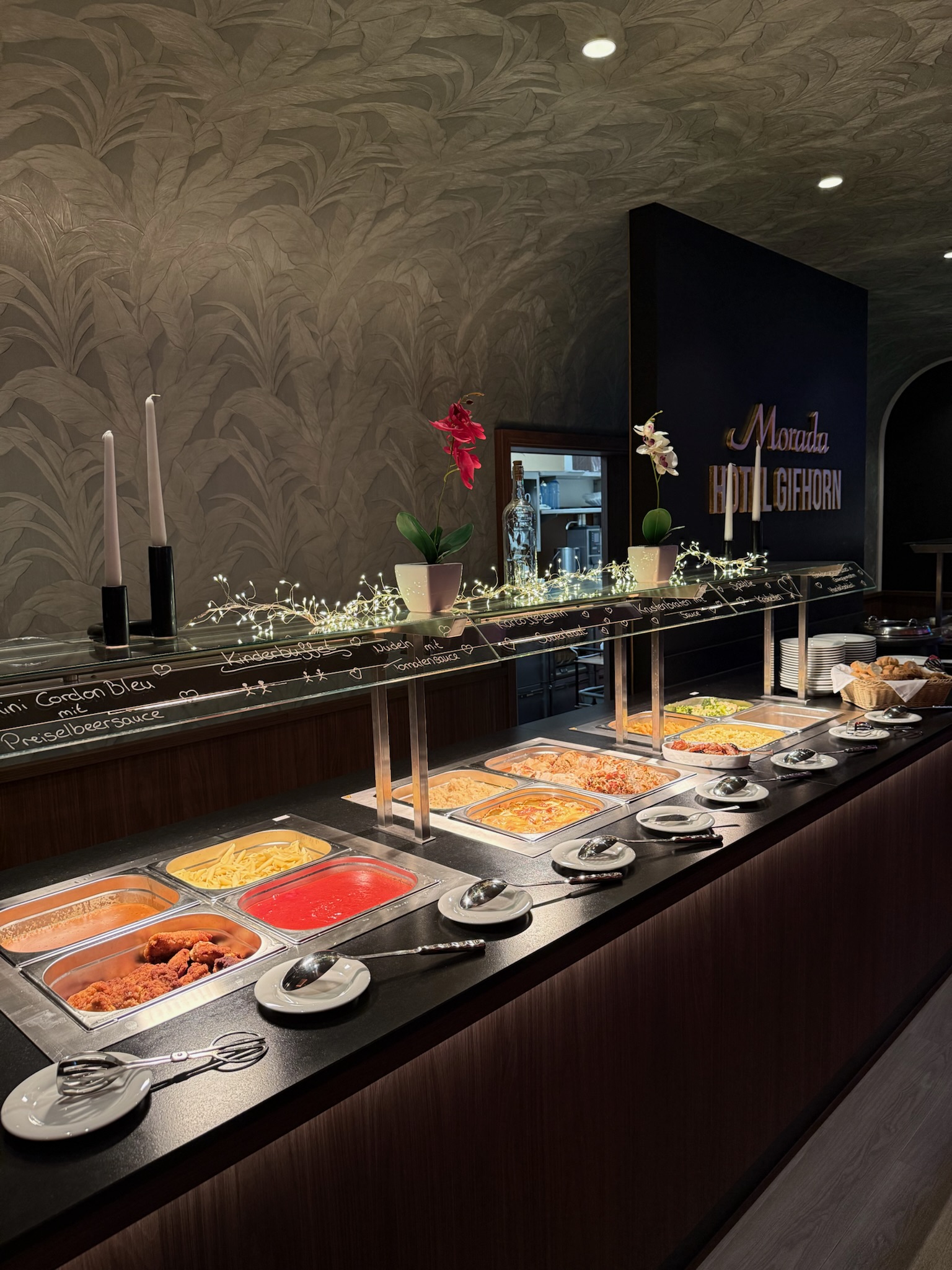 Ein Buffet mit verschiedenen warmen Gerichten, darunter Entenbrust, Kartoffeln und Kalbsgeselchtes, in Edelstahlbehältern präsentiert.