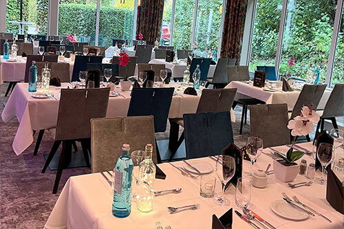 Eleganter Speisesaal mit gedeckten Tischen, weißen Tischdecken und Gläsern, geschmackvolle Dekoration mit Orchideen und Glasflaschen.