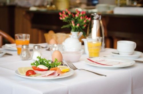 Frühstückstisch mit Aufschnitt, Ei, Saft und Kaffee, dekoriert mit Blumen