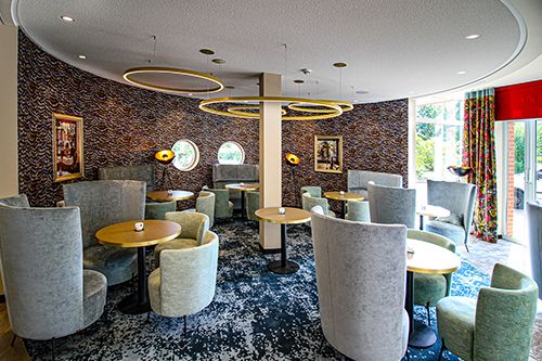 Modernes Café mit runden Tischen und abgerundeten Stühlen, dekorative Ringlampen an der Decke.