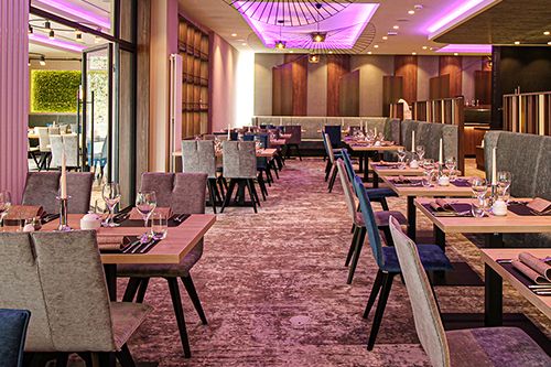 Ein stilvoll eingerichtetes Restaurant mit modernen Möbeln und lila Beleuchtung an der Decke.