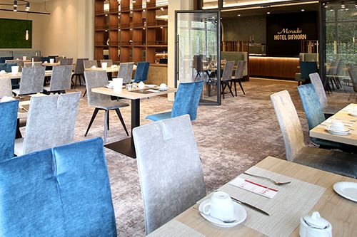 Moderner Speisesaal eines Hotels mit gedeckten Tischen und eleganten Stühlen.