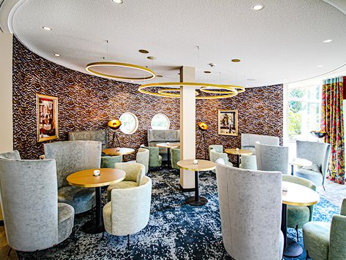 Elegantes Café mit grauen Sesseln, runden Holztischen und moderner Beleuchtung.