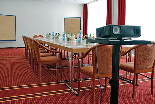 Konferenzraum mit rechteckigem Tisch, Stühlen, Getränken und einem Projektor.