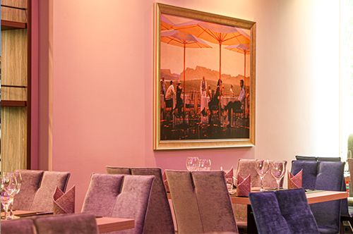 Innenansicht eines elegant eingerichteten Restaurants mit lila und grauen Stühlen, gedeckten Tischen und einem großen Wandbild von Personen auf einer Terrasse.