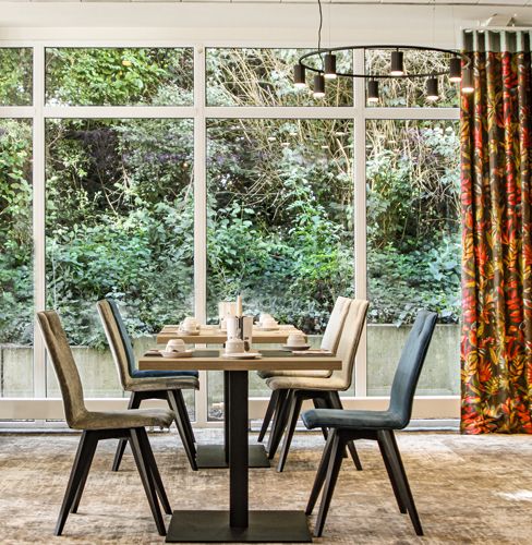 Ein modern eingerichtetes Café mit Tisch und Stühlen, das durch große Fenster einen Blick ins Grüne bietet.