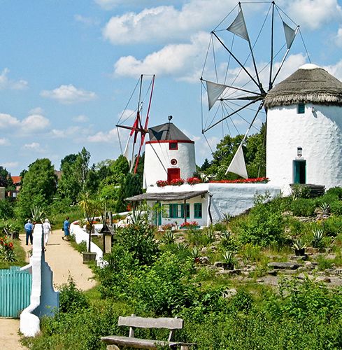 Historische Windmühlen in einer grünen Gartenlandschaft an einem sonnigen Tag.