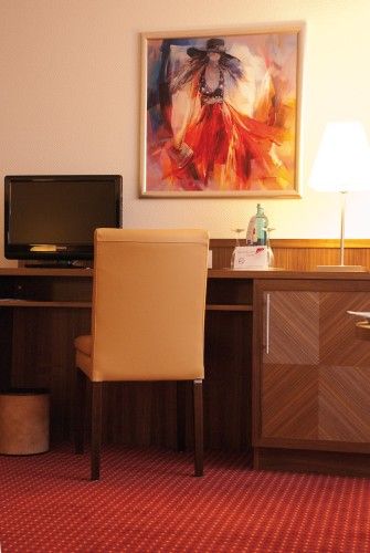Hotelzimmer-Schreibtisch mit Fernseher, Lampe, Stuhl und buntem Gemälde an der Wand.